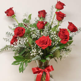 Red roses arranged in a clear glass vase with a red ribbon.
