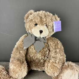 Large tan plush teddy bear with a checkered bow sitting on a wooden surface