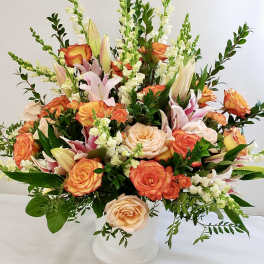 Mixed bouquet of orange and peach roses with white lilies in a white vase