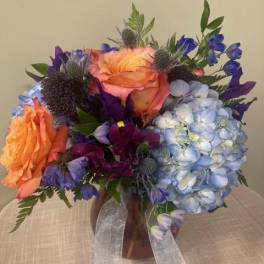 Bouquet of orange, blue, and purple flowers in a vase with ribbon