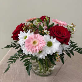 Bouquet of red roses and pink gerbera daisies in a clear glass vase