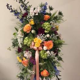 Tall standing floral spray with multicolored blooms and a pink ribbon