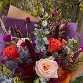 Hand-tied bouquet of coral and blush roses with purple accents