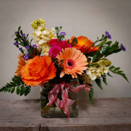 Mixed bouquet of orange and pink flowers in a glass vase with a pink ribbon