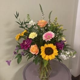 Mixed bouquet with sunflowers, roses, and gerbera daisies in a glass vase