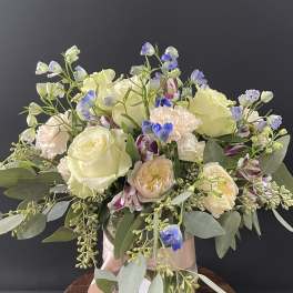 Bouquet of cream roses, pale peach blooms, and blue accents in a vase