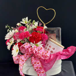 Pink and white flower arrangement with a heart topper and gift items in a round box