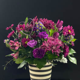 Purple and pink mixed bouquet in a striped vase with a wire heart accent