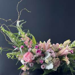 Pink and white floral arrangement with lilies and roses in a low container