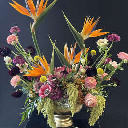 Large mixed floral arrangement with orange bird-of-paradise and pink blooms in a gold vase