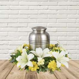 White lilies and yellow flowers arranged around a silver urn.
