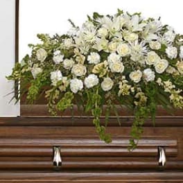 White floral casket spray with trailing greenery on a wooden casket