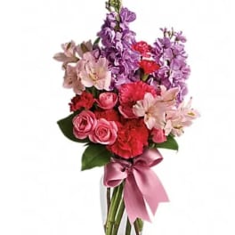 Bouquet of pink and purple flowers in a clear glass vase with a pink ribbon