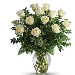 White roses arranged in a clear glass vase with mixed greenery