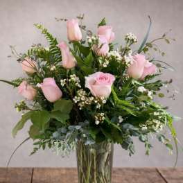 Pink roses arranged in a clear glass vase with mixed greenery.