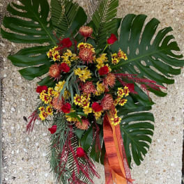 Tropical floral standing spray with red and yellow blooms and large palm leaves