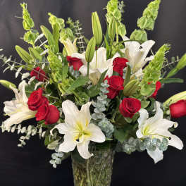 Red roses and white lilies in a clear glass vase with greenery