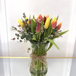 Yellow and red tulips with small white blooms in a tall clear glass vase tied with twine