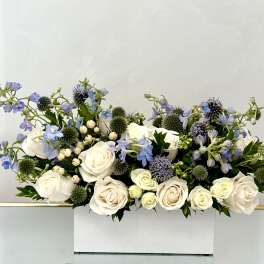 White roses and blue flowers arranged in a white box