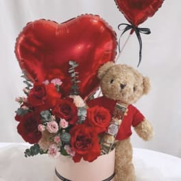 Red heart balloons with roses and a teddy bear in a pink box