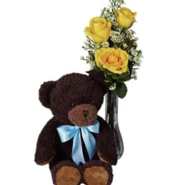 Teddy bear beside yellow roses in a glass vase