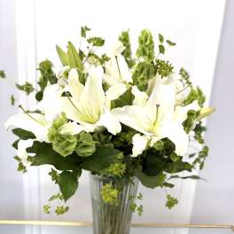 White lilies in a clear glass vase with green filler flowers