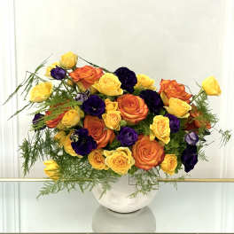 Bouquet of yellow, orange, and purple roses in a white vase