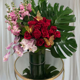 Bouquet of red roses, pink orchids, and pink stock in a dark vase