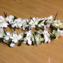 White floral lei with green leaves on a wooden surface