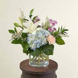 Mixed bouquet in a clear glass vase with white lilies and blue hydrangeas