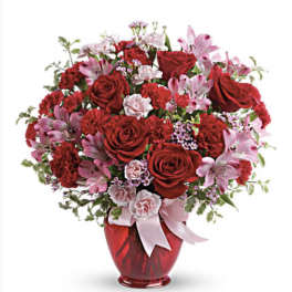 Red and pink flower arrangement in a red vase with a ribbon