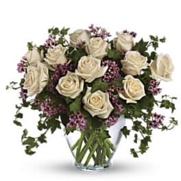Cream roses with purple filler in a clear glass vase