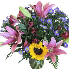 Bouquet of pink lilies, purple daisies, and a sunflower in a glass vase