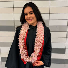 Woman in a graduation gown wearing a pink flower lei