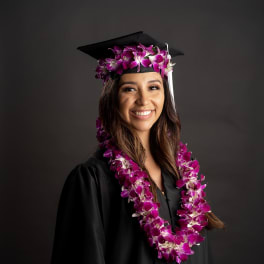 Graduate in a cap and gown wearing a purple orchid lei and matching cap flowers