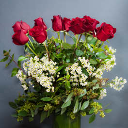 Red roses arranged in a green glass vase with white filler flowers