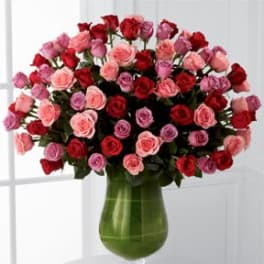 Bouquet of red, pink, and lavender roses in a green glass vase