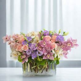 Arrangement of pink, purple, and white flowers in a clear rectangular vase