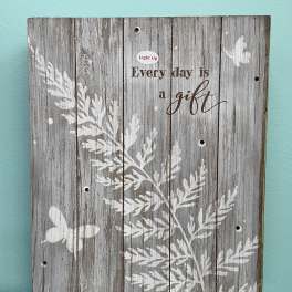 Rustic gray wooden sign with white foliage, butterflies, and the words "Every day is a gift".