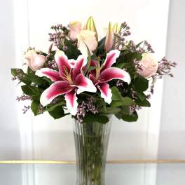 Pink lilies and pale roses in a tall glass vase