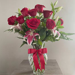 Red roses and pink lilies in a clear glass vase with a red ribbon
