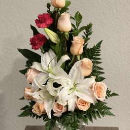 Bouquet of peach roses, white lilies, and red carnations in a glass vase