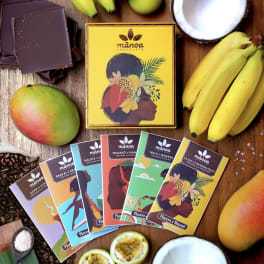 Assorted chocolate bars surrounded by tropical fruit on a wooden surface.