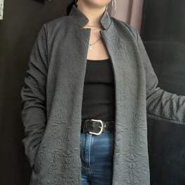 Person wearing a long textured gray coat over a black top and blue jeans