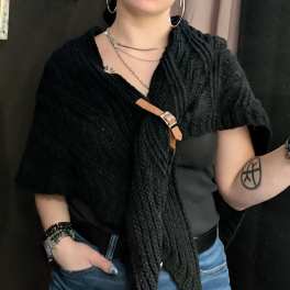 Person wearing a black textured top with a tan buckle detail and blue jeans