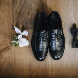 Black dress shoes with a white boutonniere and plaid bow tie