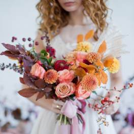 Woman holding a bouquet of peach and orange flowers with autumn leaves