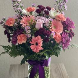 Mixed pink and purple bouquet in a glass vase with a purple ribbon