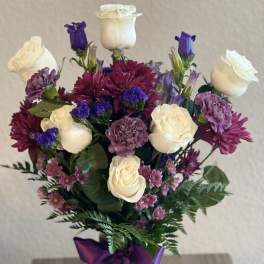 Bouquet of white roses, purple blooms, and a purple ribbon in a glass vase