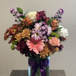 Mixed bouquet of chrysanthemums and roses in a glass vase with a purple ribbon
